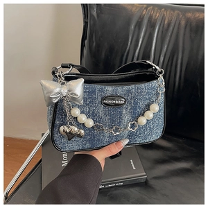 Détail du sac bandoulière en denim bleu avec nœud argenté, breloques cœur et chaîne perle