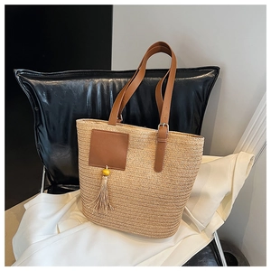 Detail of woven straw tote bag featuring brown leather handles and tassel accent