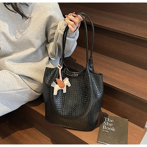 Detail of black woven tote bag with pegasus charm held by a model on wooden stairs