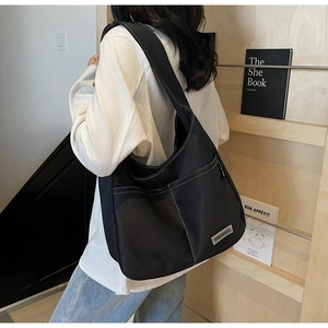 Detail of black canvas shoulder bag with white contrast stitching and outer pockets