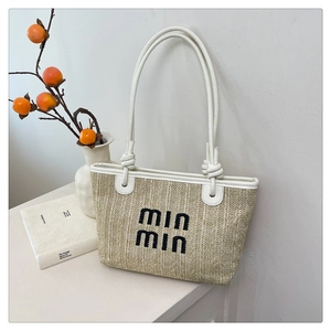 Detail shot of beige woven straw tote with black embroidered lettering and white leather handles