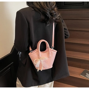 Detailed view of pink textured leather handbag featuring pearl and lace bow decorations