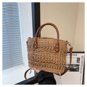 Detail of hollow-out straw tote bag with brown faux leather handles and drawstring closure