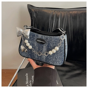 Détail du sac bandoulière en denim bleu avec perles, chaînes et un nœud en satin