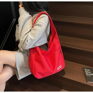 Detail of red canvas hobo shoulder bag with MERREY brand label on a wooden staircase