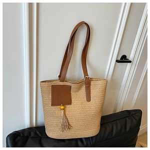 Detail of straw woven tote bag featuring dark brown PU straps and yellow beaded tassel