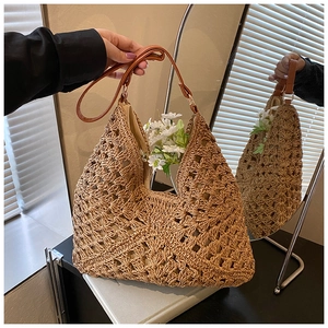 Detail view of woven straw tote bag featuring brown faux leather strap and golden ring