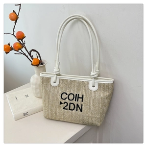 Detail of woven straw tote bag with white leather straps and black embroidered letters