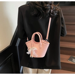 Detail of pink lychee leather bucket bag with pearl and lace bow charm on model