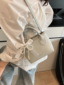 Chic light blue bucket bag with pearl and bow charm on a minimalist indoor model view