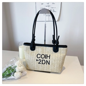 Detail of woven straw tote bag with black COIH 2DN embroidery and knotted handles