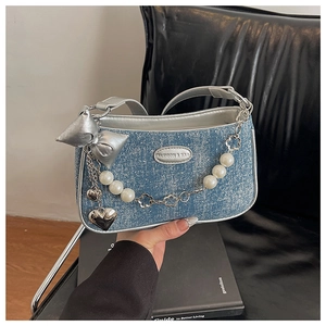 Détail d'un sac en jean bleu clair avec breloque noeud argenté et chaîne de perles