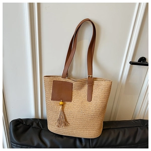 Close-up of the large woven straw tote bag featuring leather straps and a decorative tassel