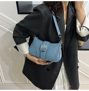 Close-up of denim shoulder bag with silver buckle strap and delicate metal chain detail