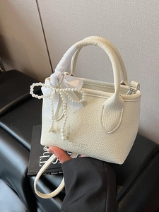 Elegant off-white bucket bag with litchi texture, ribbon detail, and pearl bow ornament