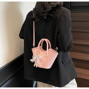 Detail of pink pebbled leather handbag with pearl and lace bow charm on model