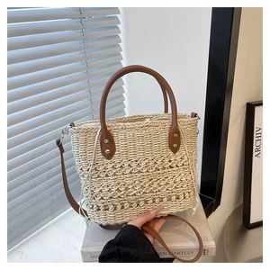 Detailed macro of woven straw tote bag with brown faux leather handles and silver rivets