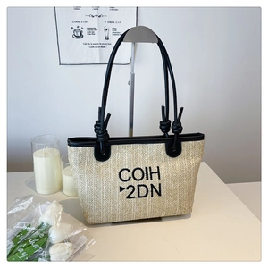 Detail shot of the woven straw tote bag with black letter embroidery and leather handles