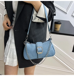 Detail of light blue denim shoulder bag featuring a silver chain and large decorative buckle