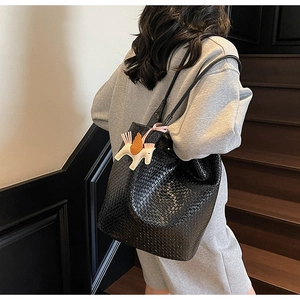 Detail of black woven leather tote bag with a decorative horse charm on model