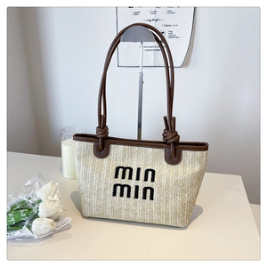 Detail of woven straw tote bag with brown leather straps and black min min embroidery
