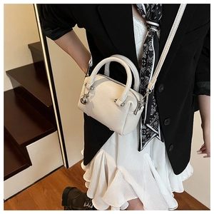 Détail du sac Boston en cuir litchi blanc avec breloque cloche et bandoulière réglable