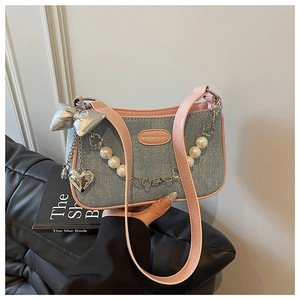 Détail du sac bandoulière en denim bleu avec bord rose et breloques en perles