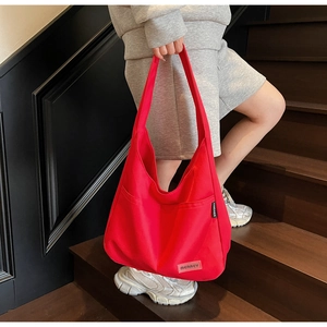 Detail of red canvas tote bag showing wide shoulder strap and brand label on vintage stairs