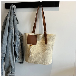 Detail of hand-woven straw tote bag with brown leather handle and boho tassel detail