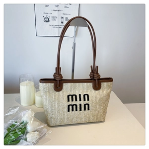 Detail of woven beige tote bag featuring black logo embroidery and brown leather knot handles