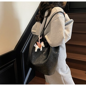 Detail of a black woven leather tote bag with a pegasus charm worn on a shoulder