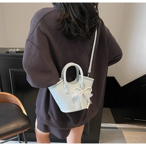 Detail of light blue textured tote bag with elegant pearl lace bow charm on model