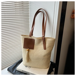 Detail of beige woven straw tote bag with brown leather straps and stylish tassel charm