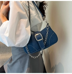 Detailed view of dark blue denim underarm bag with silver chain and metal buckle