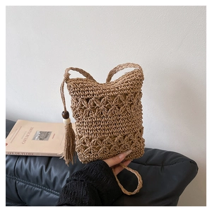 Detailed view of handmade woven straw bucket bag with floral patterns and tassel charm