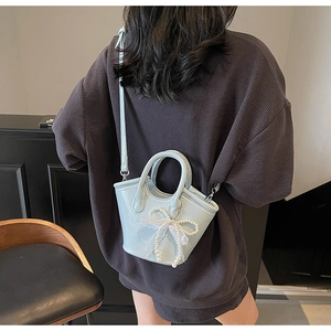 Detailed texture of mint green crossbody bag with pearl bow decoration on model