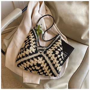 Detail of geometric crochet straw tote with black faux leather strap on a beige suit