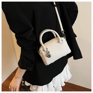 Sac Boston blanc avec texture litchi et pendentif argenté porté en bandoulière par le modèle