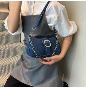 Close-up of blue denim baguette bag featuring silver metal buckle and chain decoration