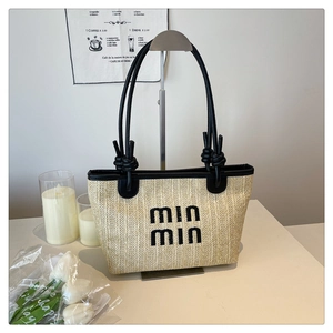 Detail of woven straw tote bag featuring black leather handles and knotted strap design