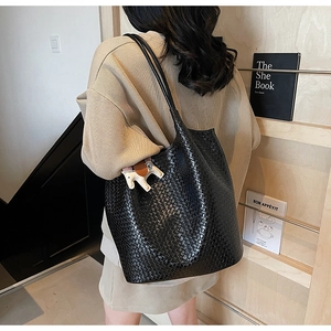 Detail of black woven leather tote bag with thin straps and a horse-shaped decorative charm