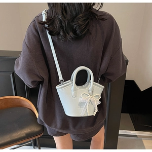 Detail of light blue crossbody bag with pearl bow charm worn by a model in casual setting