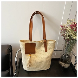 Detail of straw tote bag featuring brown leather straps and decorative tassel ornament