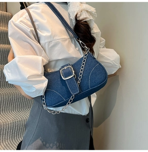 Detail of dark blue denim underarm bag with white stitching and silver metal chain strap