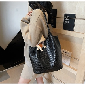 Close-up of black woven tote bag featuring a decorative horse charm on a shoulder strap