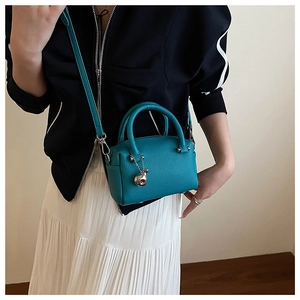 Détail du mini sac Boston en cuir litchi bleu lac avec pendentif métallique élégant