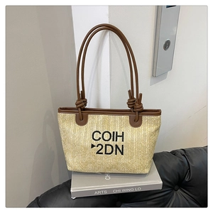 Detail of beige woven tote bag with black letter embroidery and brown leather straps