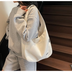 Close-up of off-white nylon tote bag with front pocket and woven logo on wood stairs
