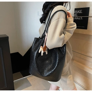 Detail of black woven texture tote bag featuring a decorative cream horse charm