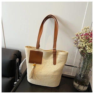 Close-up of straw woven tote bag featuring brown leather straps and tassel detail